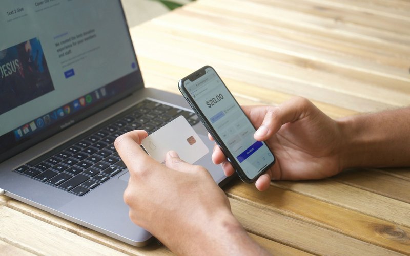 Une personne tient une carte bancaire et un smartphone affichant un paiement, devant un ordinateur portable.