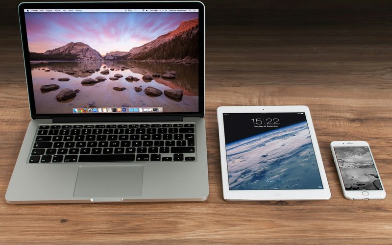 Un ordinateur portable, une tablette et un smartphone allumés côte à côte sur un bureau en bois.