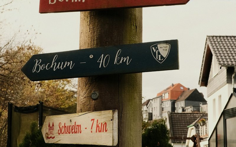 Panneaux de signalisation en bois fixés sur un même poteau, indiquant plusieurs villes et directions différentes.