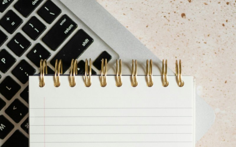 Un carnet à spirale posé sur le clavier d'un ordinateur portable, illustrant la coexistence des méthodes papier et numérique.