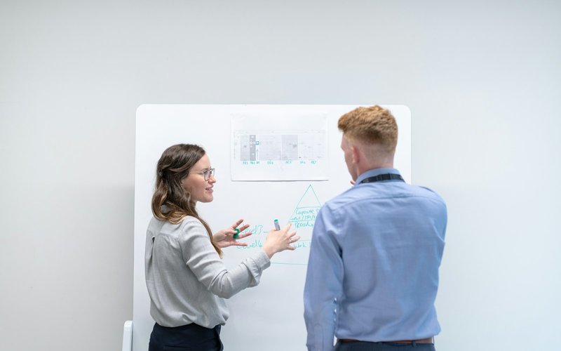 Deux collègues discutent devant un tableau blanc.